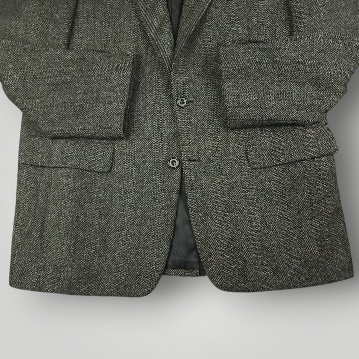 Close-up of a gray herringbone tweed jacket with large flap pockets and front buttons